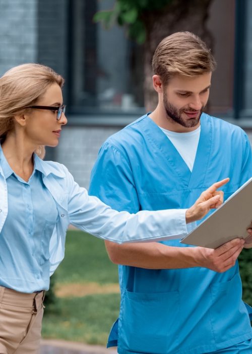 teacher of medical university pointing on something in notebook to student on street